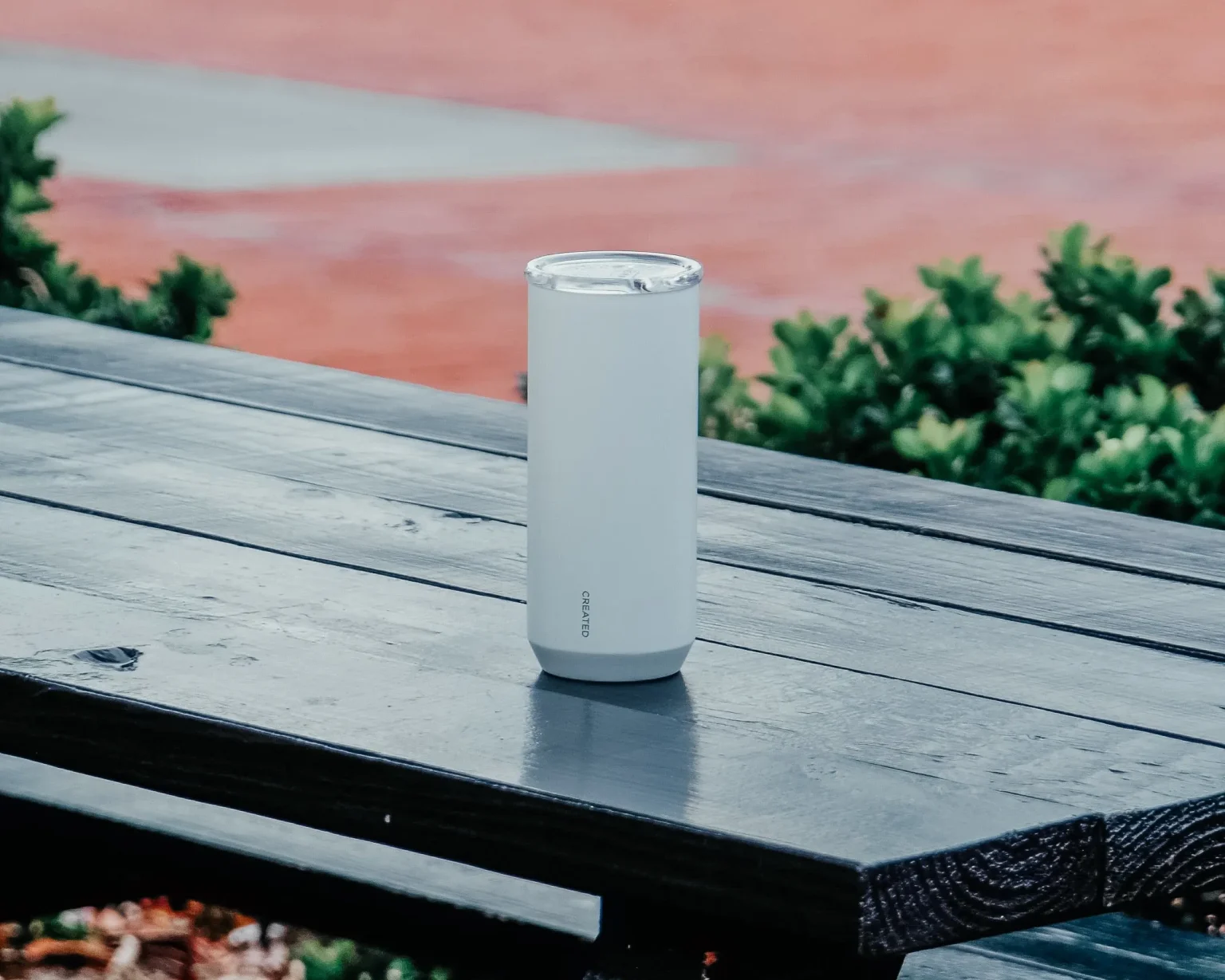 A sleek, minimalist white Created Co. tumbler sitting on a wooden picnic table.