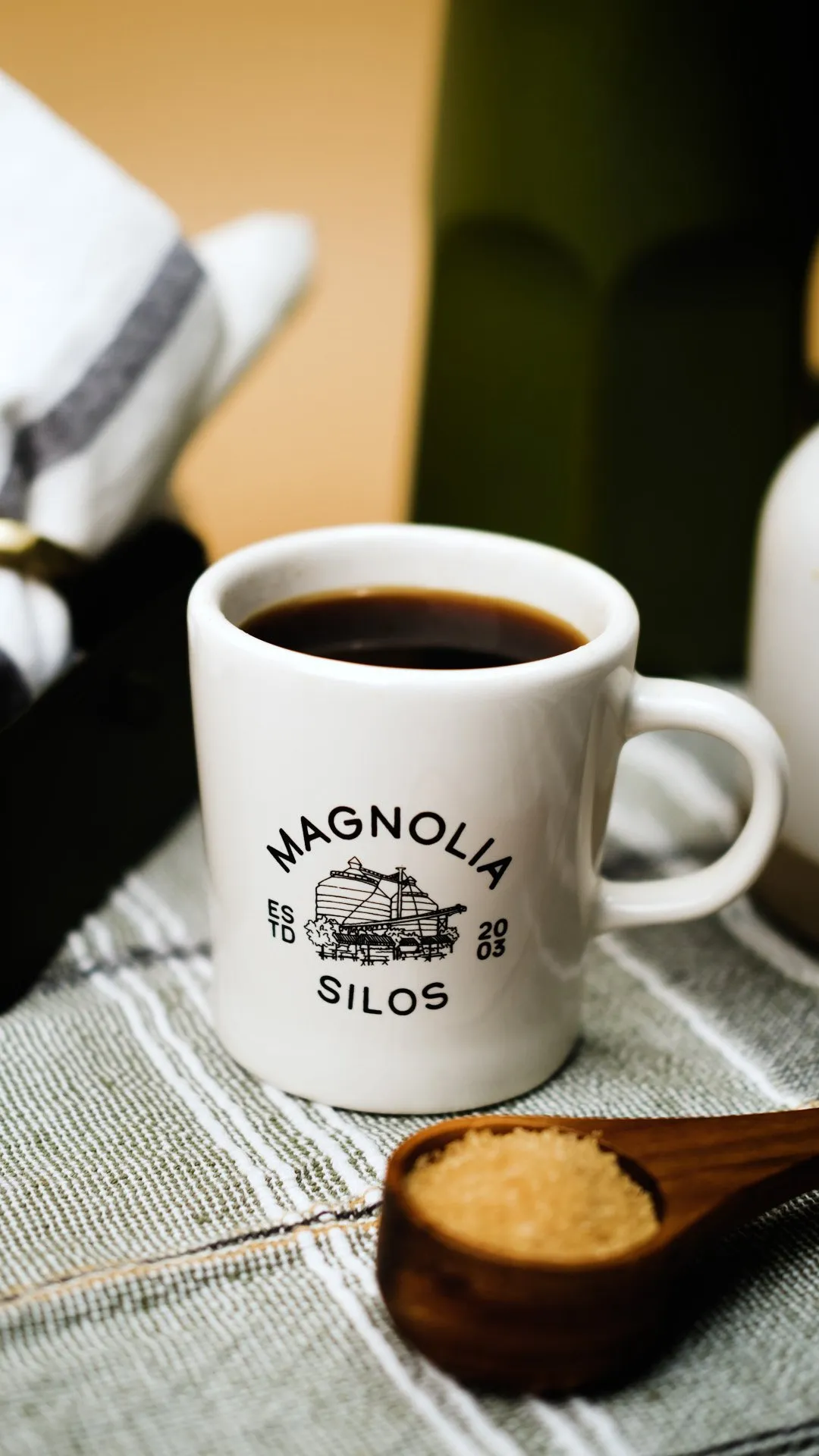 A classic white diner mug filled with coffee, a scoop of brown sugar, and a MAGNOLIA SILOS logo.
