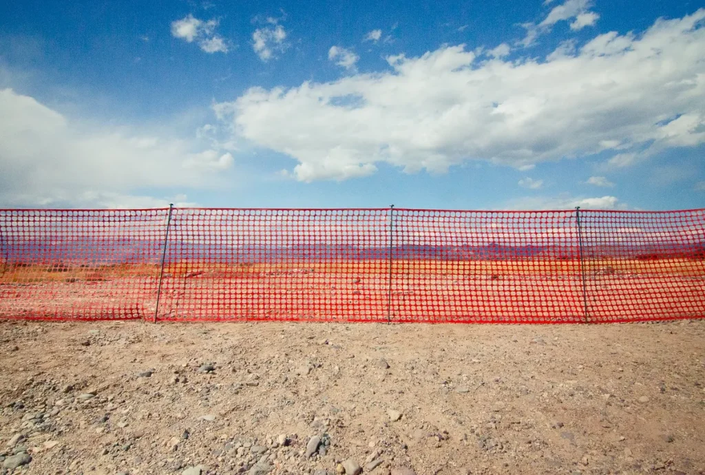 A traditional orange plastic safety fence stretches across a barren desert landscape, symbolizing the outdated and inefficient methods commonly used for site security.